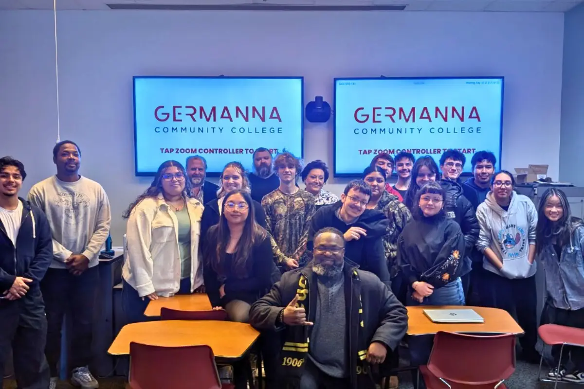 A group of Germanna Community College students and an adult male standing together in front of school desks and two screens.
