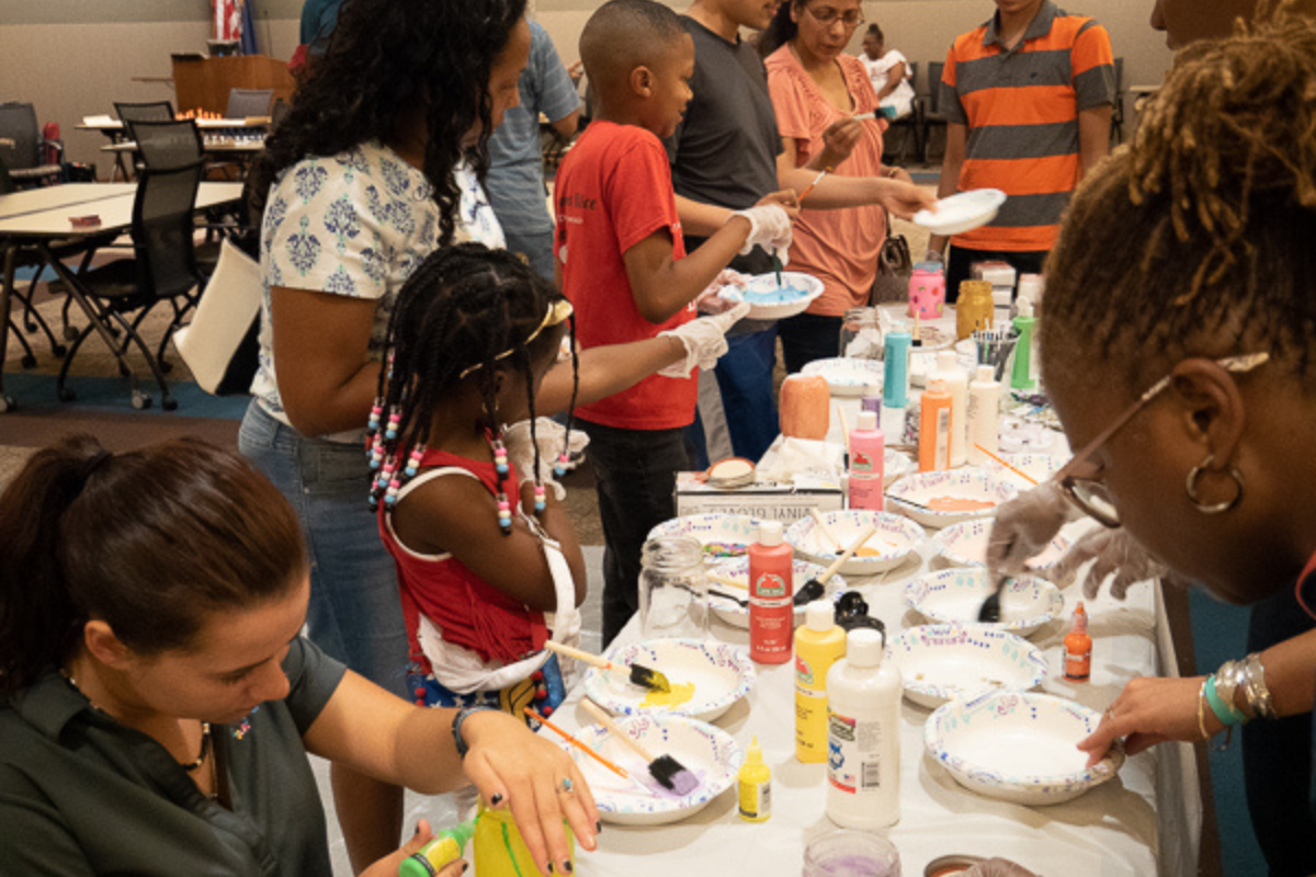 A group of children and adults standing around a table with bowls of paint and paintbrushes.